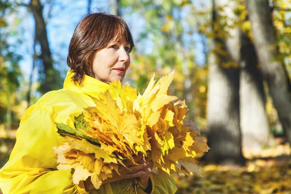 Belle femme plus âgée tenant une feuille d'érable tombée — Photo