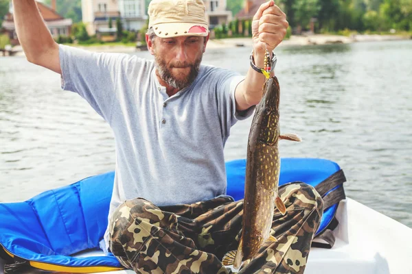 Fisherman sitting in boat and keeps caught pike — Stock Photo, Image