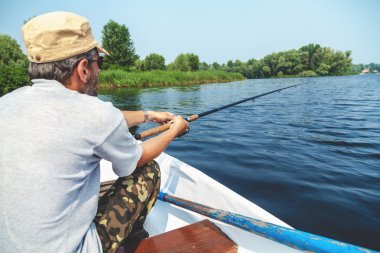 Balıkçı tekne içinde oturan ve olta tutan sakallı