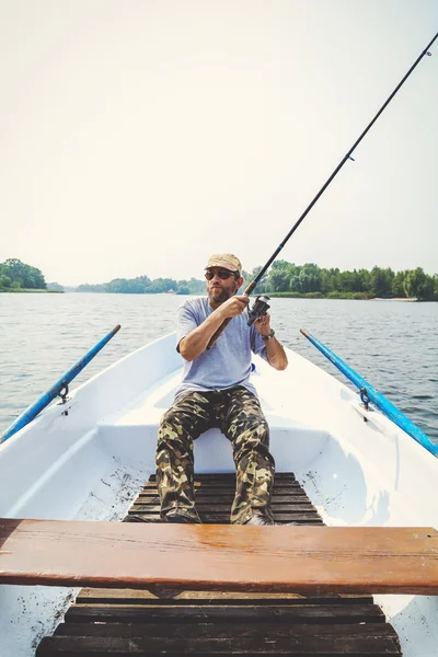 Fisherman with beard sitting in boat and holding fishing rod — Stock Photo, Image