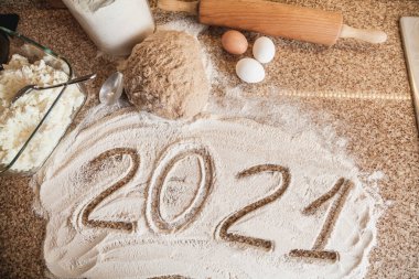 Mutfakta yeni yıl. 2021 un ile yazılmıştır. Granit tezgahın üzerinde bir parça hamur, yumurta ve ahşap bir oklava yatıyor.
