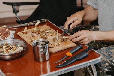Toplanan mantarların incelenmesi. Tahta bir yaban domuzunun üstünde yenebilir mantar kesen bir adamın elleri.