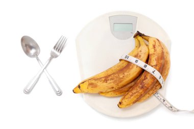 Bir grup olgun muz plastik pulların üzerinde yatıyor. Muza sarılmış santimetre. Çatal ve kaşığın yanında.