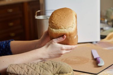 Kadın elleri elektrikli ekmek makinesinin ekmek pişirme kalıbından taze ekmek tutar. Yakınlarda büyük bir bıçak var.