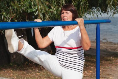 Nehir kıyısında jimnastik. Sevimli yaşlı kadın metal barda sağlık egzersizleri yapıyor.
