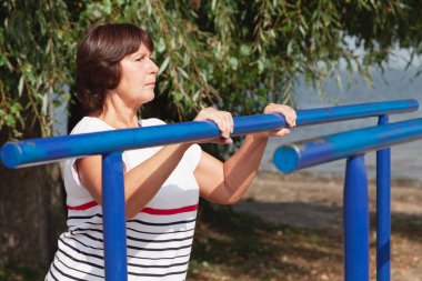 Nehir kıyısında jimnastik. Sevimli yaşlı kadın metal barda sağlık egzersizleri yapıyor.