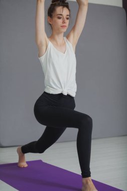 Uzun bir elbise giyerek uzun süre saçlarını toplamış güzel bir kız ve parlak bir kanguru ile yoga yapıyor.