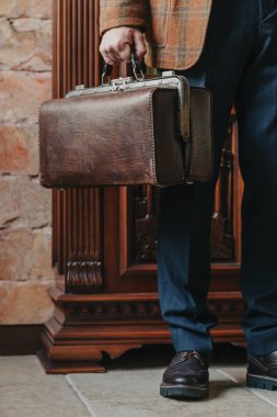 Katı mavi pantolonlu bir adamın sol elinde klasik deri çanta.