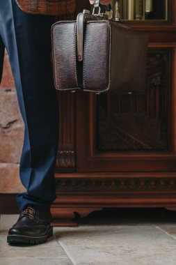 Katı mavi pantolonlu bir adamın sol elinde klasik deri çanta.