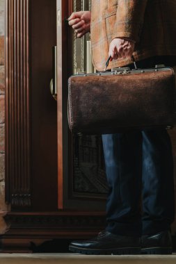 Usta saatçi antika bir büyükbaba saatinin kapısını açar. İçinde aletler olan bir valiz taşıyor.