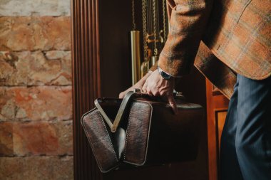 Gösterişli ekose ceketli bir beyefendi, evdeki eski moda bir çantayı açıyor.