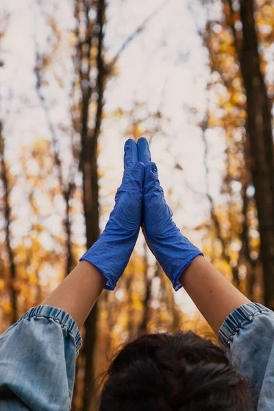 Pleading in the forest. A man raised his hands in blue rubber latex disposable  gloves up and folded his palms together in the autumn forest close-up