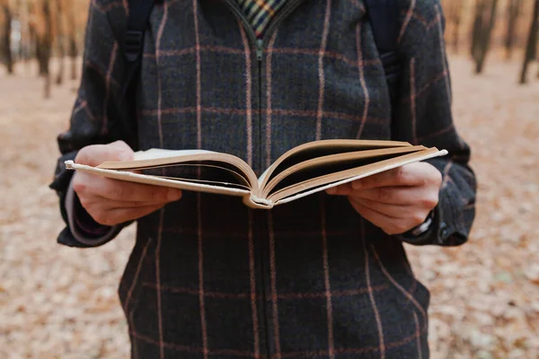 Man in a plaid jacket reading a book in the autumn fores