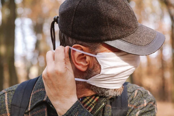 man in a cap puts on a white medical mask in the autumn fores