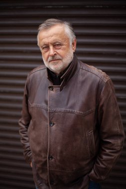 Gri sakallı bir adamın portresi. Bir sonbahar günü deri ceketli yaşlı bir adamın yakın çekimi. Arka Yuvarlanan Kapı