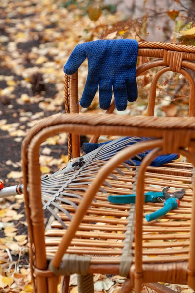 秋天的平静生活 秋天的公园里 一把扇子耙和一把花园剪子躺在一把漂亮的柳条椅子上 旁边是蓝色手套 Close — 图库照片