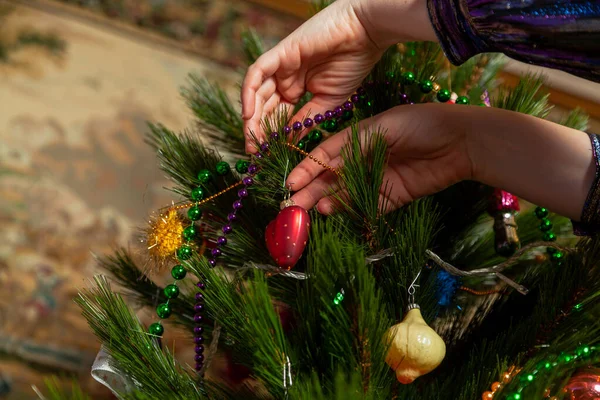 We decorate the Christmas tree. A hand hangs an original toy in the form of a red heart on a green branch of a Christmas tre