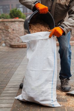 Atık topluyoruz. Adam kovadan ahşap talaş dökerek plastik torbaya koyuyor.
