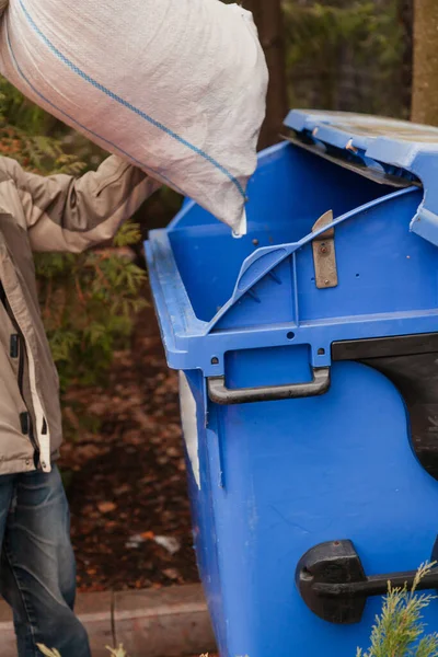 我们在垃圾箱里收集垃圾 人把装好的包放在蓝色的垃圾箱里 — 图库照片
