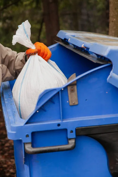 We collect garbage in the bin. Man puts filled bag in blue garbage containe