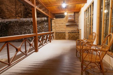Verandada kış akşamı. Boş bir verandada oturan iki tahta hasır sandalye. Korkuluklarda ve yerde beyaz kar var. İki kolye ışığı parlıyor