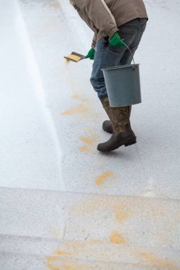 Buzla savaşıyor. Lastik çizmeli bir adam kaygan bir kış yoluna küçük bir kürek ve bir kova ile kum serpiyor.