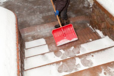 Kırmızı plastik kürek, tuğla bir merdivenin basamaklarından kar kürekliyor. Yukarıdan Görünüm