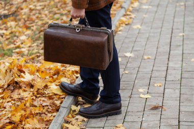 Şık bir ceketi olan beyefendi sonbahar öğleden sonra meydanın ortasında duruyor. Elinde kaliteli bir halı çantası tutuyordu. Kapat.