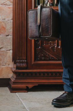 Katı mavi pantolonlu bir adamın sol elinde klasik deri çanta.