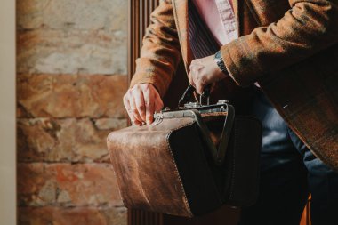Gösterişli ekose ceketli bir beyefendi, evdeki eski moda bir çantayı açıyor.