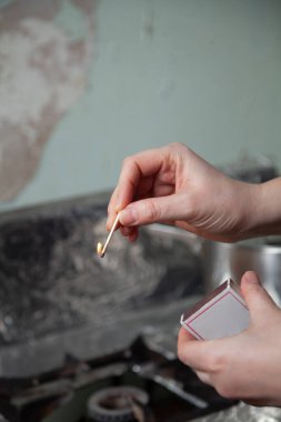 Sağ elinde yanan bir kibrit tutuyor. Sol elinde bir karton kibrit kutusu var.