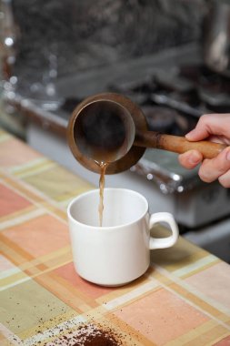 Doğal kahve yaparız. Pirinç hindiden gelen kahveyi beyaz bir fincana döküyorum. Kareli masanın üzerine öğütülmüş kahve serpilmiş.