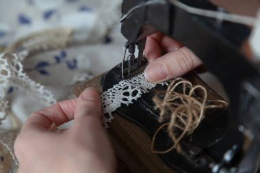 El yapımı terzi. İnce parmaklı kadın örgüyü yakın plan dikiş makinesinde tutuyor. Yakınlarda mavi bir kumaş var.