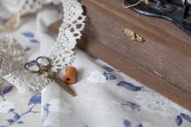 İnce dantel örgü ve sarı vintage makas mavi çiçek desenli beyaz kumaşın üzerinde yatar. Yakınlarda ahşap bir kutu ve kakao var.