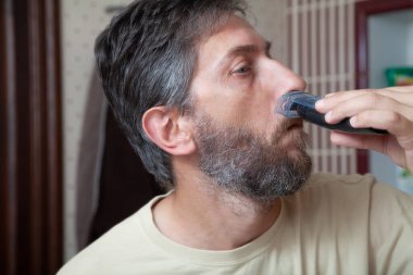 Saç kesim sakal kesme makinesi. Gri sakalını tek başına kesen bir adam hortumu kapalı bir makine kullanıyor.