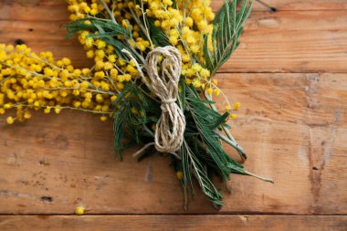 Bahar etüdü. Sarı mimozanın bir dalı tahta tahtalarda yatar. Üstte numara şeklinde bir ip var. 