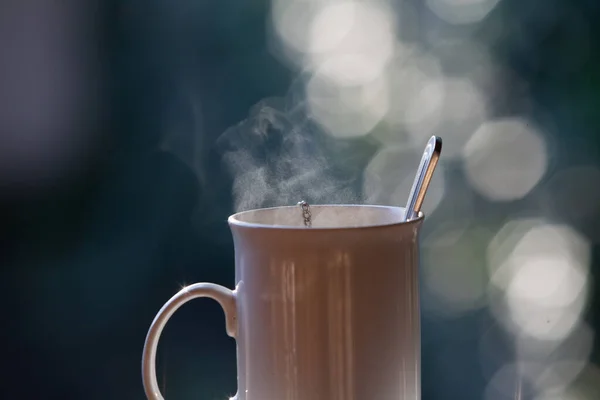 Strict tall white cup with a comfortable handle on a gray blurred background. Around the blurry glare of light. In a cup a spoo