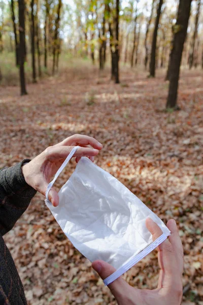 Viral safety in the forest. Hands hold a white medical mask in front of them in the spring forest. Close-u