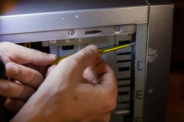 Bilgisayar tamiri. Eller bir bilgisayar kutusundaki vidayı yakın çekim tornavidayla söker.