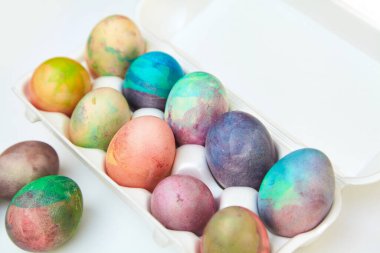 Paskalya tatiline özen göster. Farklı renklerde boyanmış birkaç tavuk yumurtası hücreli plastik bir kapta bulunur. Yakınlarda üç yumurta var.