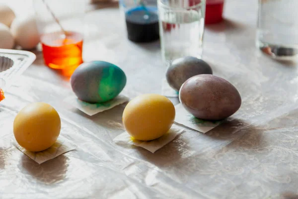 On the home table, a creative mess was lit when painting Easter eggs. Paints and tools of the artist are randomly laid out. Next to some painted egg