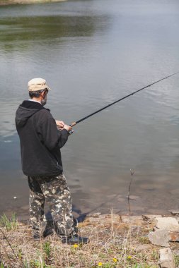 Ceketli bir adam, sonbaharda bir su deposunun kıyısında dönen bir çubukla balık tutuyor.