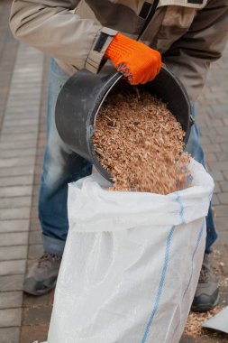 Atık topluyoruz. Adam kovadan ahşap talaş dökerek plastik torbaya koyuyor.
