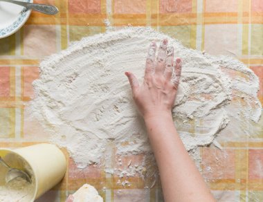 Ev sahibesinin sağ eli kareli masa örtüsünün üzerindeki beyaz unu eşitliyor. Yukarıdan bak. Fotoğraf smartphon ile çekildi