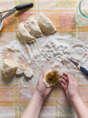 Hamur köftesi yapıyorum. Elleri dolgulu bir hamur parçası tutuyor. Yanında üç tane çiğ hamur köftesi ve un var. Yukarıdan bak. Fotoğraf smartphon ile çekildi