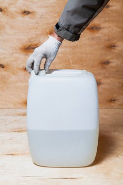 Beyaz eldivenli bir el, beyaz plastik bir kutunun kapağını kontrplağın arka planına doğru açar. Konteynır likörle dolu.