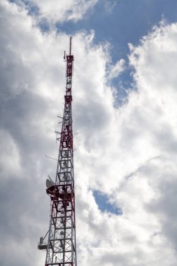 Televizyon sinyali iletimi için uzun metal kafes kulesi beyaz bulutların arkasında duruyor. Alt yaşam
