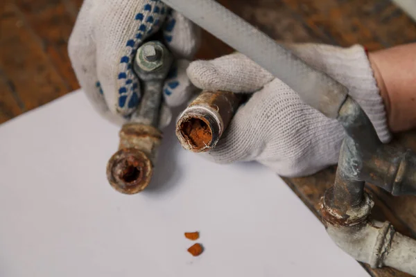 Awful condition of the old water pipe. Hands in work gloves hold pieces of an old pipe. A layer of rust is visible inside. Close-u