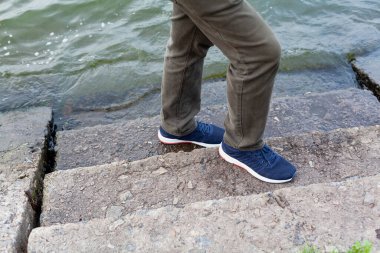 Mavi ayakkabılı ayaklar, yumuşak, taştan bir merdivenin üzerinde duruyor. Alt basamaklar nehir suyuyla yıkanır.