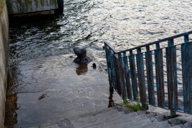 Dar, yumuşak eğimli taş merdiven beton bir iskeleye iniyor. İskelede tek bir kazık var. Sağdaki metal bir korkuluk. Yukarıdan Görünüm